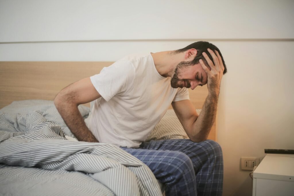 man holding head sitting on a bed after too much fitness training